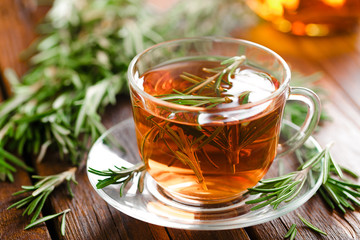 Rosemary tea in glass tea cup on rustic wooden table closeup. Herbal vitamin tea.