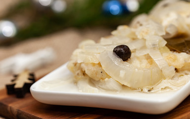 Fish in vinegar on white plate with Christmas decorations in the background