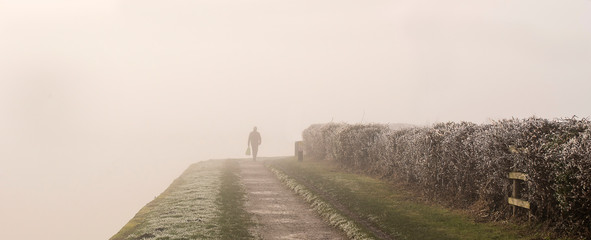 Distant figure walking on a canal towpath in thick fog