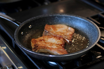 Pork chops frying in a pan on a stove top.
