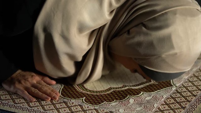 Woman in hijab prostrating on prayer rug, obligatory religious ritual, worship
