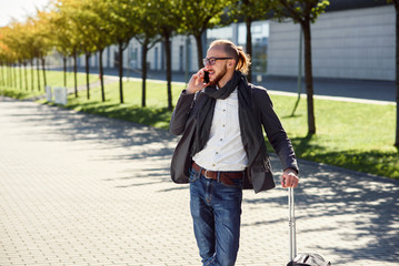 Successful businessman in casual suit pulls a suitcase, hurries to the airport and talks on smart...