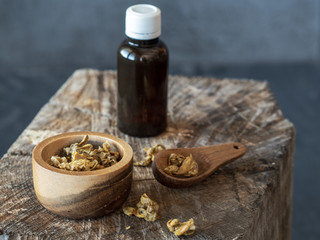 A bottle of propolis and wooden bowl and spoon of propolis granules on piece of wood.