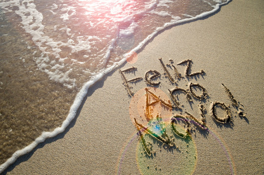 Portuguese Feliz Ano Novo (Happy New Year) message handwritten in textured lettering on smooth sand with a fresh new wave on a Brazilian beach