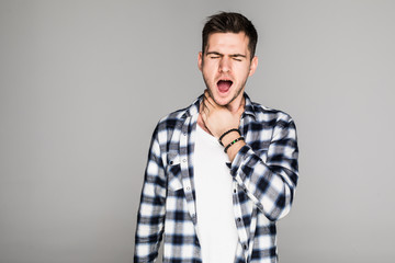 Young man having sore throat and touching his nec against grey background. Hard to swallow