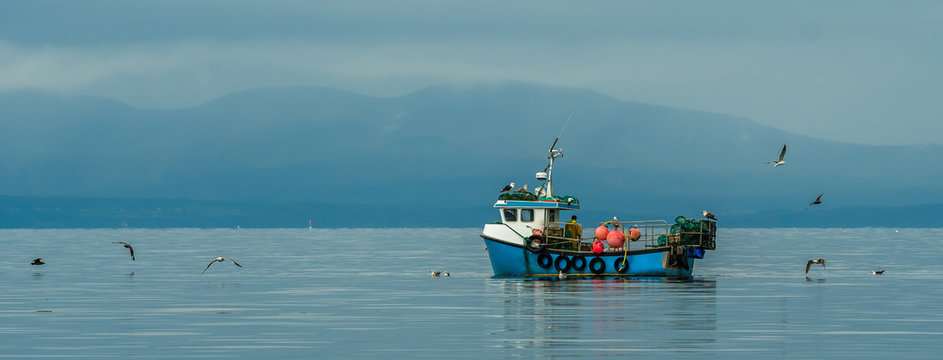 Small Fishing Boat With Lobster Pods And Seagulls On Calm Atlantic In Front Of The Hebride Islands