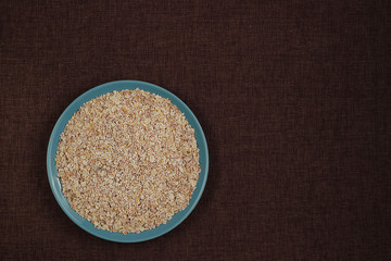 Raw oat flakes cereals in blue plate on dark rustic canvas background top view