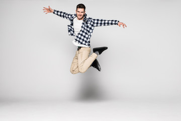 Full length portrait of a casual young man jumping with hands outstretched isolated over white...