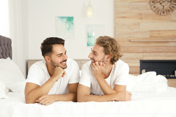 Happy gay couple lying on bed at home