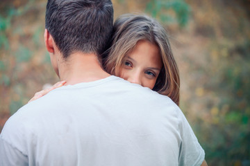 Obraz premium A girl with beautiful blue eyes hugs a boy. Happy lovers. A woman with long hair looks out from behind a man’s shoulder. A weak woman trusts a man. Valentine's Day.