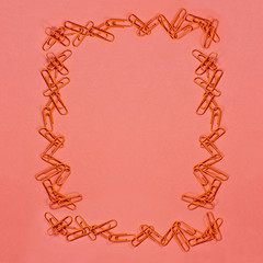 Orange paper clip frame over coral color paper background with free space for text. Image shot from above.