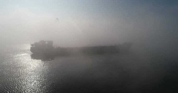 A huge barge on the river Dnipro in the morning fog with a visible silhouette of the buildings and city in the background (shot from the air) in 4K 3