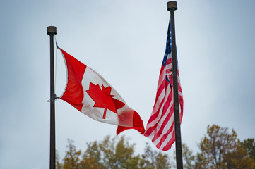 Close-up view of an American flag and a Canadian flag waving in the wind.