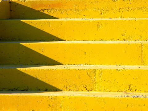 Brightly lit yellow concrete staircase, with shadows on the left side