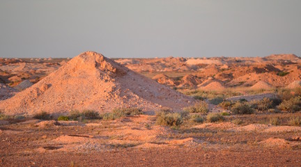 Large mounds of mine tailings in the outback Australian desert outside opal mining town of Coober Pedy at sunset