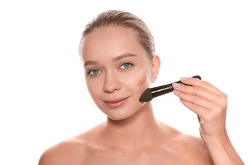 Fototapeta premium Young woman applying foundation on her face against white background