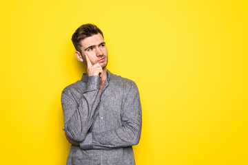 Fototapeta premium Close up portrait of thoughtful man who looks away touching his chin and weighs the pluses and minuses of the offer isolated on bright yellow background with copy space for text