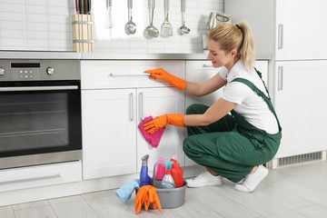 Female janitor cleaning cabinet with rag in kitchen