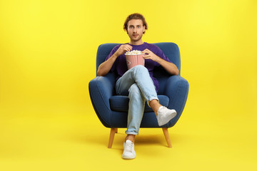 Fototapeta na wymiar Man with popcorn sitting in armchair during cinema show on color background