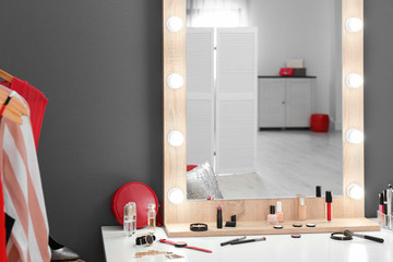 Table with makeup products and mirror near grey wall. Dressing room