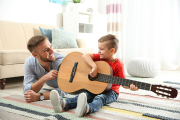Father teaching his little son to play guitar at home