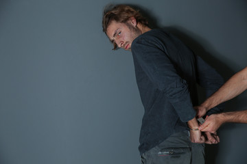 Man putting handcuffs on drug dealer against grey background. Space for text