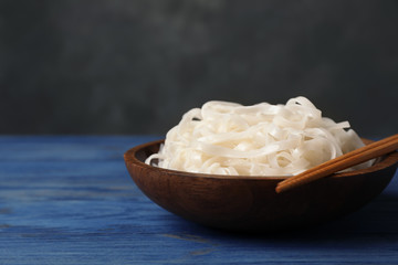 Bowl with rice noodles on wooden table. Space for text