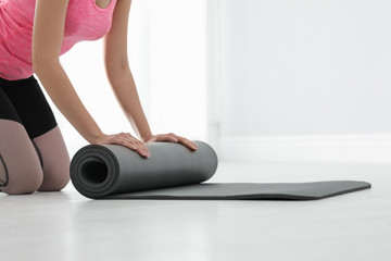 Fototapeta premium Young woman rolling yoga mat indoors, closeup. Space for text