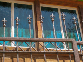 colored glass window in a wooden door behind a decorative wrought iron gate with fleur de lis finials