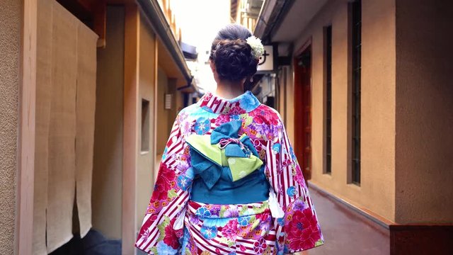 back view of young japanese girl in colorful kimono walking in path. female in traditional costume going to join festival in summer under sunshine. beautiful elegant lady in hanamikoji dori.