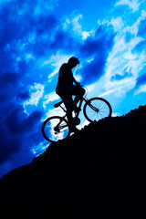 Silhouette of a boy riding a mountain bike at blue moon sky