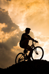 Obraz premium Silhouette of a boy riding a mountain bike at sunset
