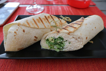 Two mexican fresh chicken and salad tortilla wraps on black plate with glasses in background
