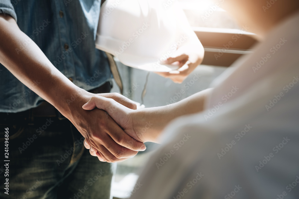 Wall mural Engineers or architecture shaking hands at construction site for architectural project, holding safety helmet on their hands.