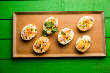 Fried hot boiled egg masala is a popular healthy breakfast or starter menu from India. With onion, coriander, black pepper, tomato and salt sprinkled over half of eggs