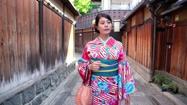 young lady with colorful flower pattern kimono dress walking in old street in ishibe alley. girl in japanese traditional costume walking in town with wooden style house surrounding stone road.