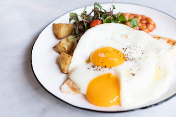 Delicious English breakfast with two fries eggs, beans, and salad on marble table.