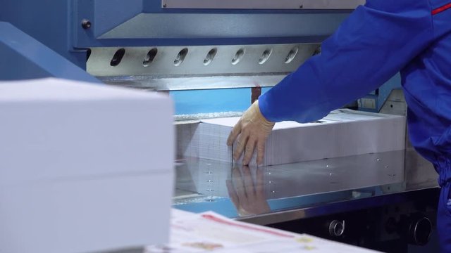 man working at print house. back view worker wearing blue uniform works with print equipment newspaper on the conveyor