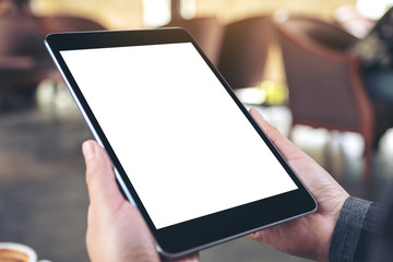 Mockup image of woman's hands holding black tablet pc with blank screen with coffee cup on wooden table in cafe