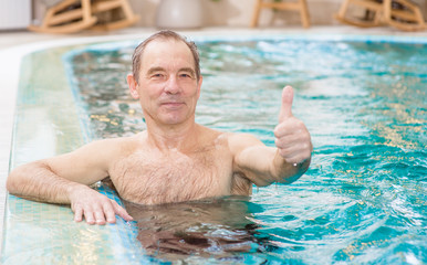 Fototapeta premium Smiling senior man in the pool showing thumbs up