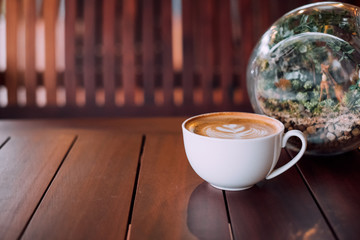 Hot Latte coffee cup heart shape on wood table with bottle garden