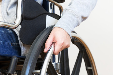 Detail of disabled woman holding a hand on wheel of a wheelchair.