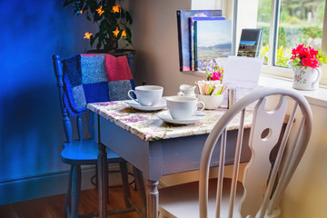 Two chairs and a table with two white cups near  a window
