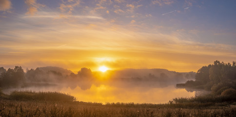 Fototapeta na wymiar fairytale misty morning by the lake. Golden fog surrounding the lake