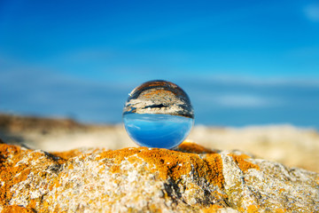  Upside down seascape with blue sky and overgrown with moss rocks - reflection in a lensball - selective focus, space for text