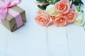 Lovely soft orange pink color rose tied by pink ribbon and brown gift box on white wood table background, sweet valentine present concept
