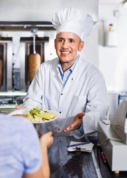 Mature man chef wearing uniform giving kebab plate to customer