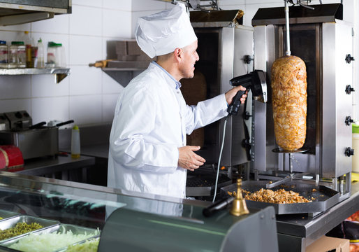 man chef wearing uniform cutting meat for kebab on kitchen in fast food restaurant