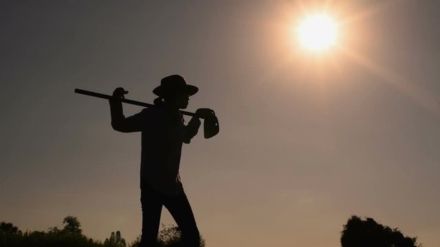 Agriculture life Concept : Black silhouette of a worker holding spade is digging soil at sunset light. Asian farmer holding spade and digging the soil.