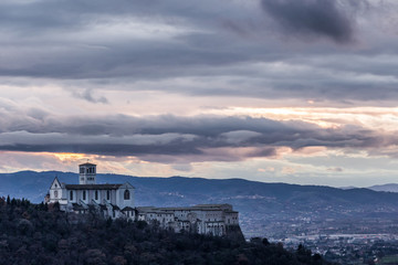 Beautiful view of St.Francis church in Assisi town (Umbria, Italy) from an unusual place at sunset, with moody clouds in the sky